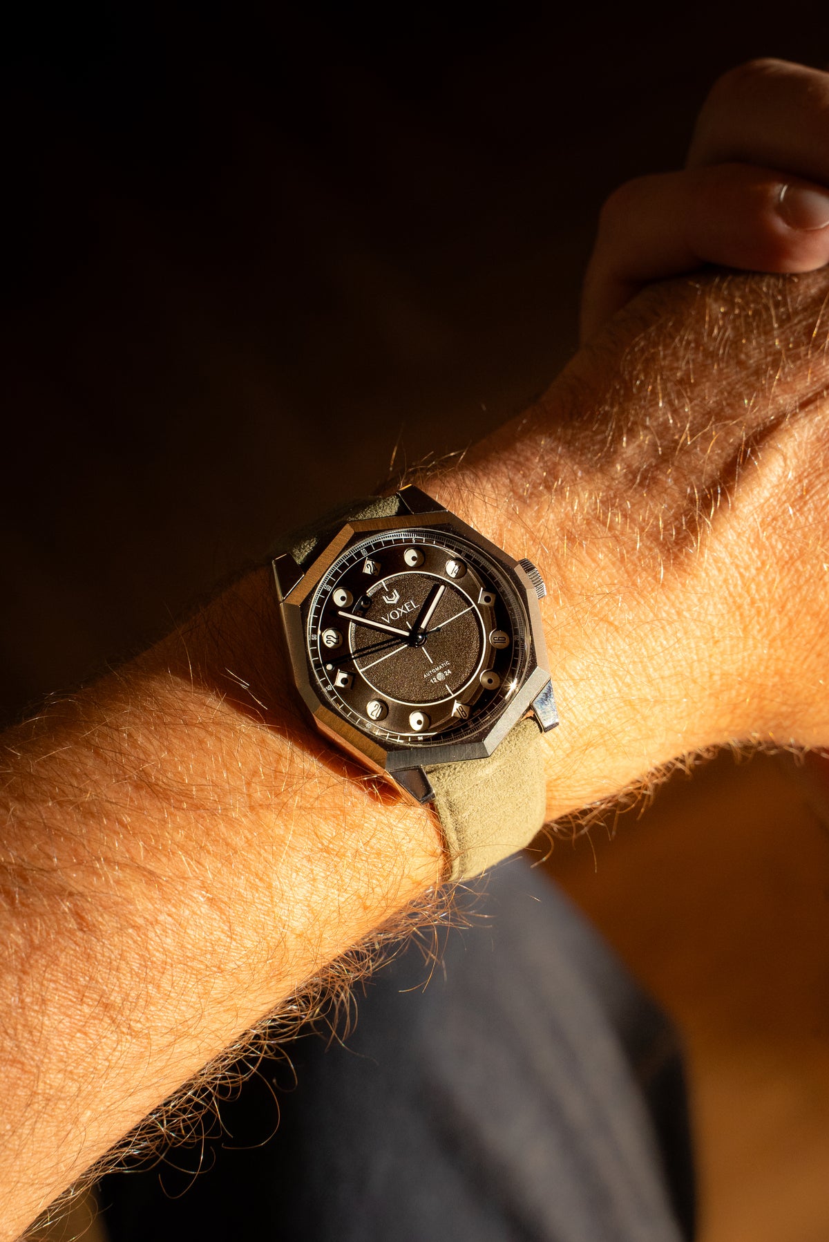 VOXEL watch on a wrist, with a dark textured dial, octagonal steel bezel and beige canvas strap, in warm sunlight